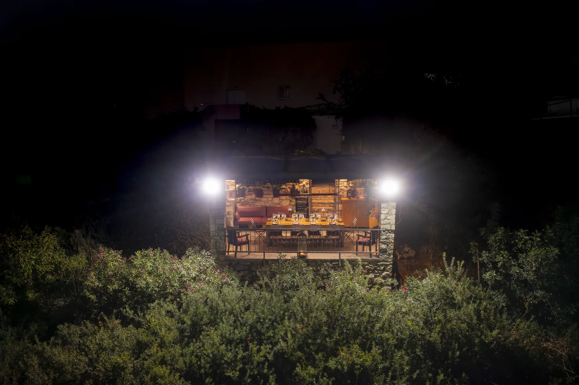 Nighttime view of a wine tasting balcony surrounded by lush vegetation, illuminated with lights.