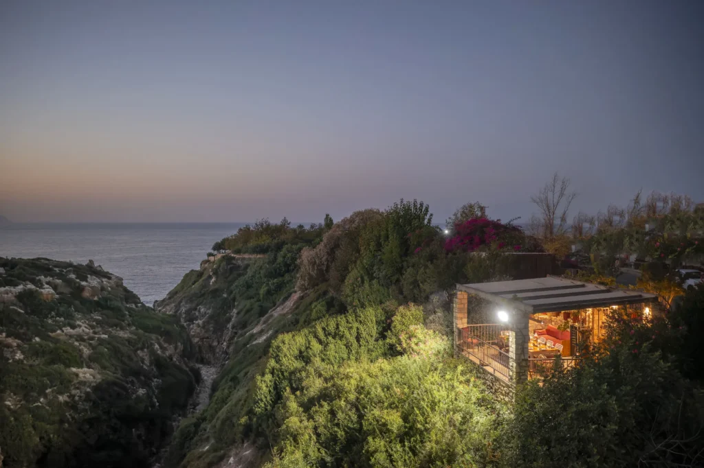 A balcony for wine tasting, surrounded by greenery, illuminated at evening, with a view of Zourida Gorge in Rethymno and the sea.