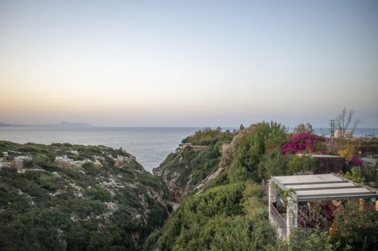 Drone shot of wine tasting balcony inside Cretan gorge surrounded by vegetation with sea view.